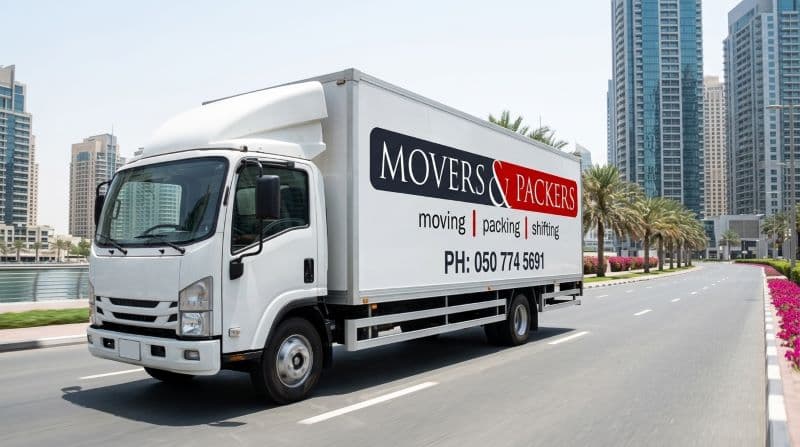 Movers and Packers UAE branded white enclosed moving truck on Dubai Marina road with company logo and phone number on side panel